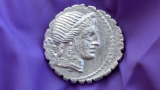 A close up of a silver coin with a Roman face