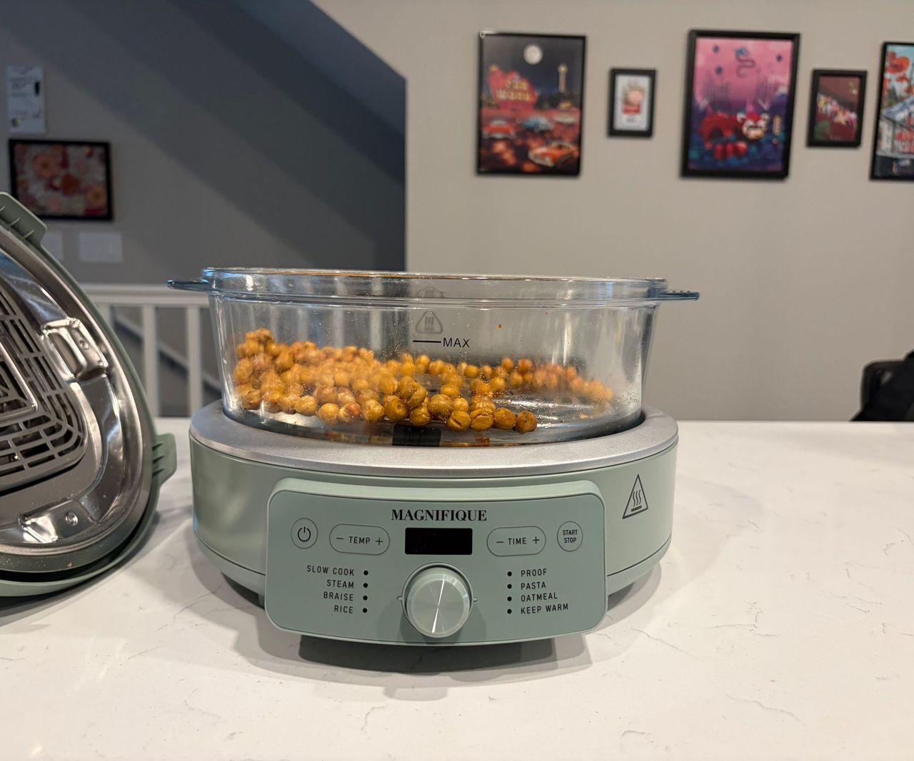 A glass air fryer with a green base on a white countertop filled with chickpeas.