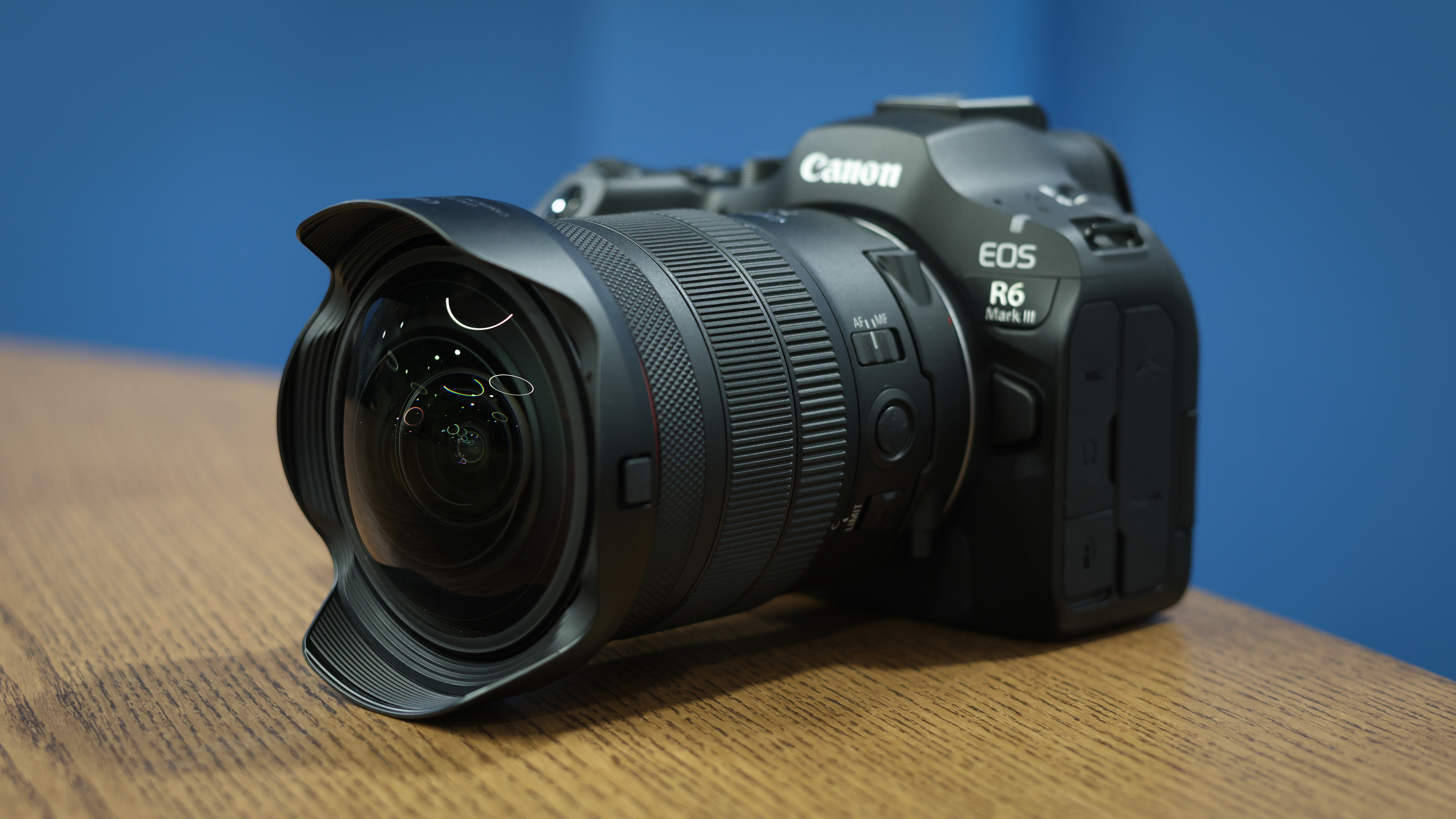 Canon RF 7-14mm f/2.8-3.5L Fisheye STM on a wooden surface in front of a blue background