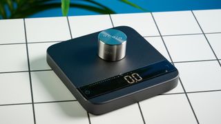 the acaia lunar coffee scale in black with an aluminum surface and accurate precise weight ideal for espresso machines given its compact size is photographed againt a blue tom's guide background