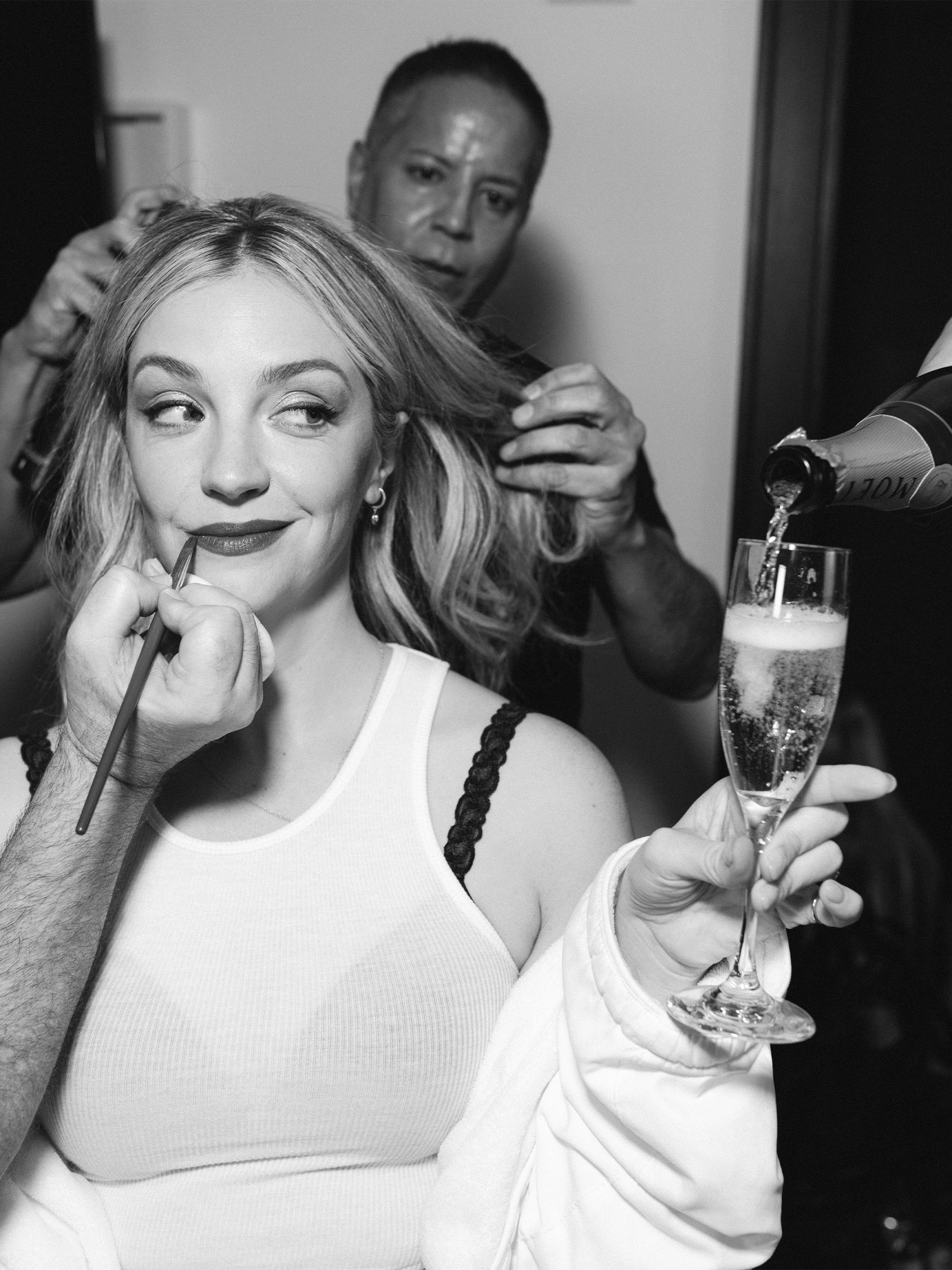 Photo of Abby Elliott from Who What Wear&#039;s Getting Ready With Me story. In the image, she is getting hair and makeup done while holding a glass of champagne.