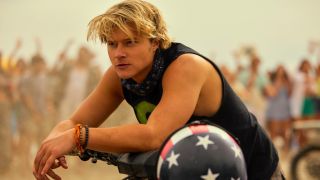 Rudy Pankow as JJ leaning over a motorcycle in Outer Banks.