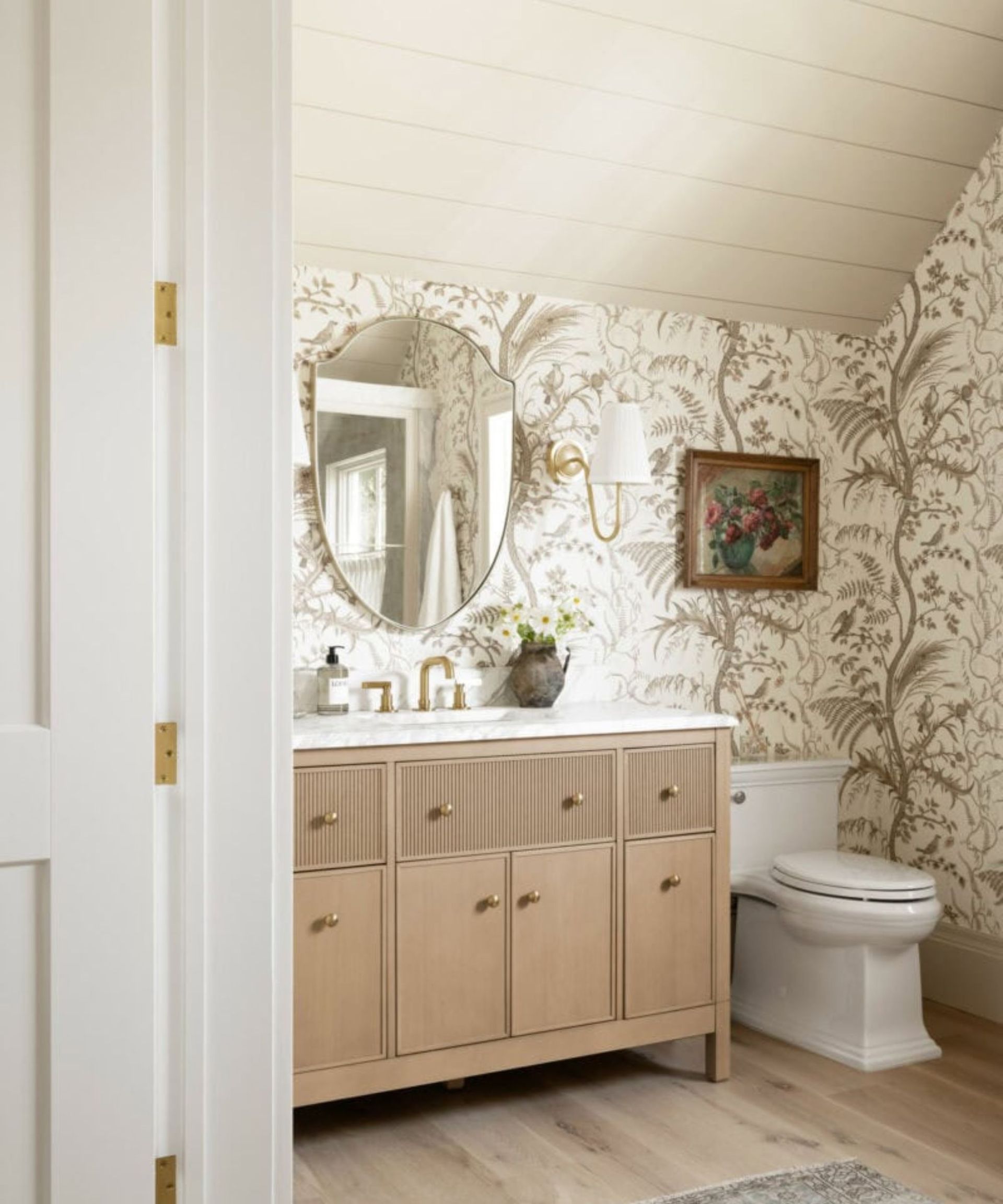 Wallpapered bathroom with wood and marble sink vanity unit and large mirror with wall sconces