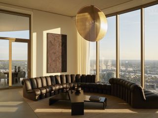 A living space with a large brown curved leather sofa and floor to ceiling windows with skyline views