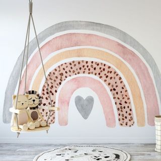 Wooden floor room with a rainbow wall decal wth a wooden hanging swing with toys and a circle carpet