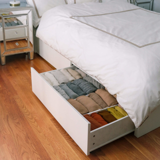 Under bed storage drawer neatly arranged with color-coordinated sweaters.