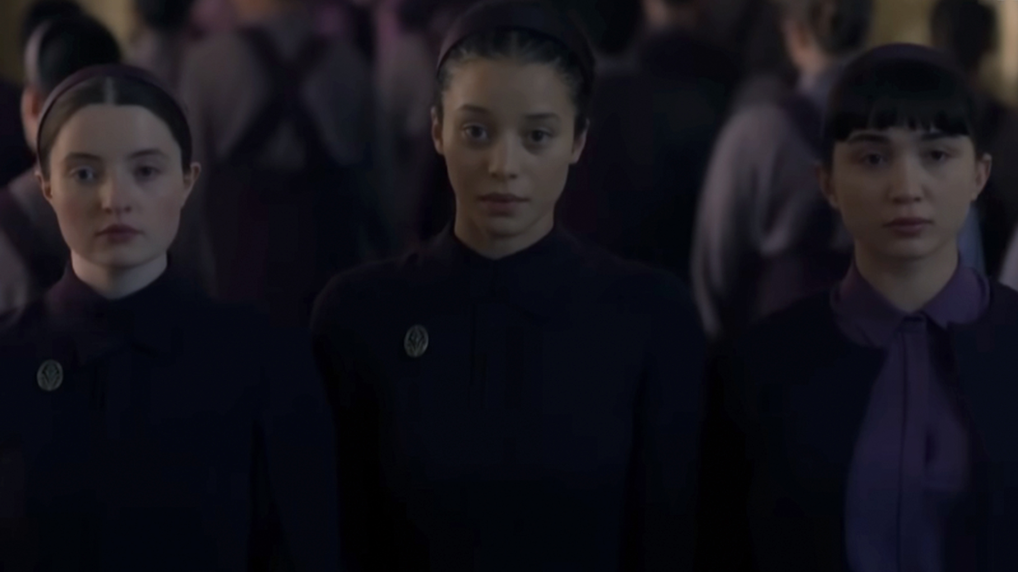 Chase Infinite looking towards the camera with other cast members in The Testaments