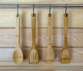 A set of wooden kitchen utensils hanging from a silver utensil rod against a wooden wall