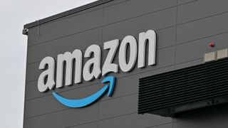 The Amazon logo, with a blue arrow rather than orange, displayed on the side of a large warehouse building