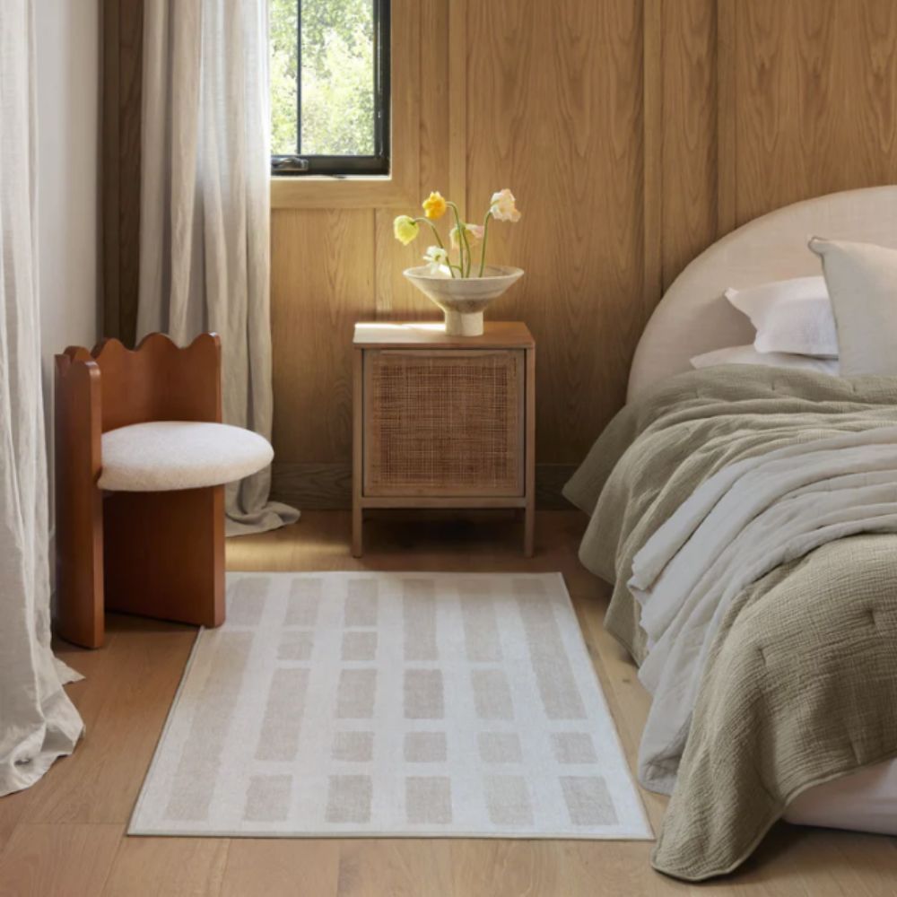 Neutral geometric rug in wooden bedroom with vase of daffodils on bedside table