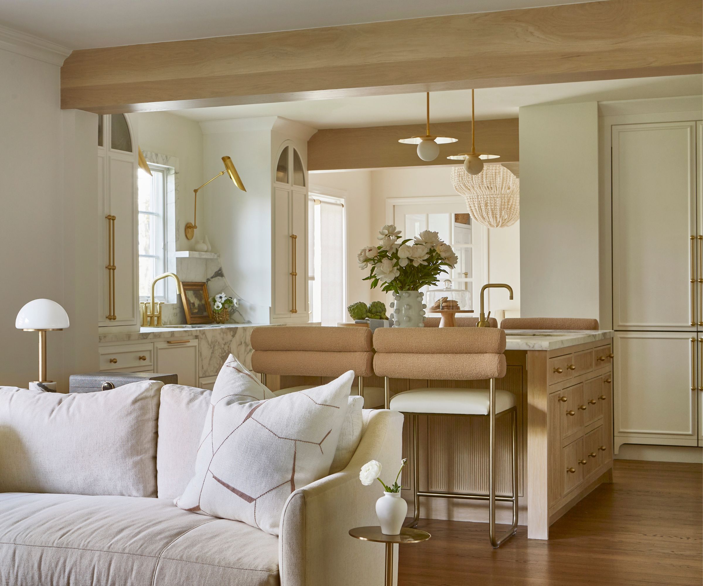 An open plan kitchen with white cabinets, a wooden island, marble countertops, and brass hardware
