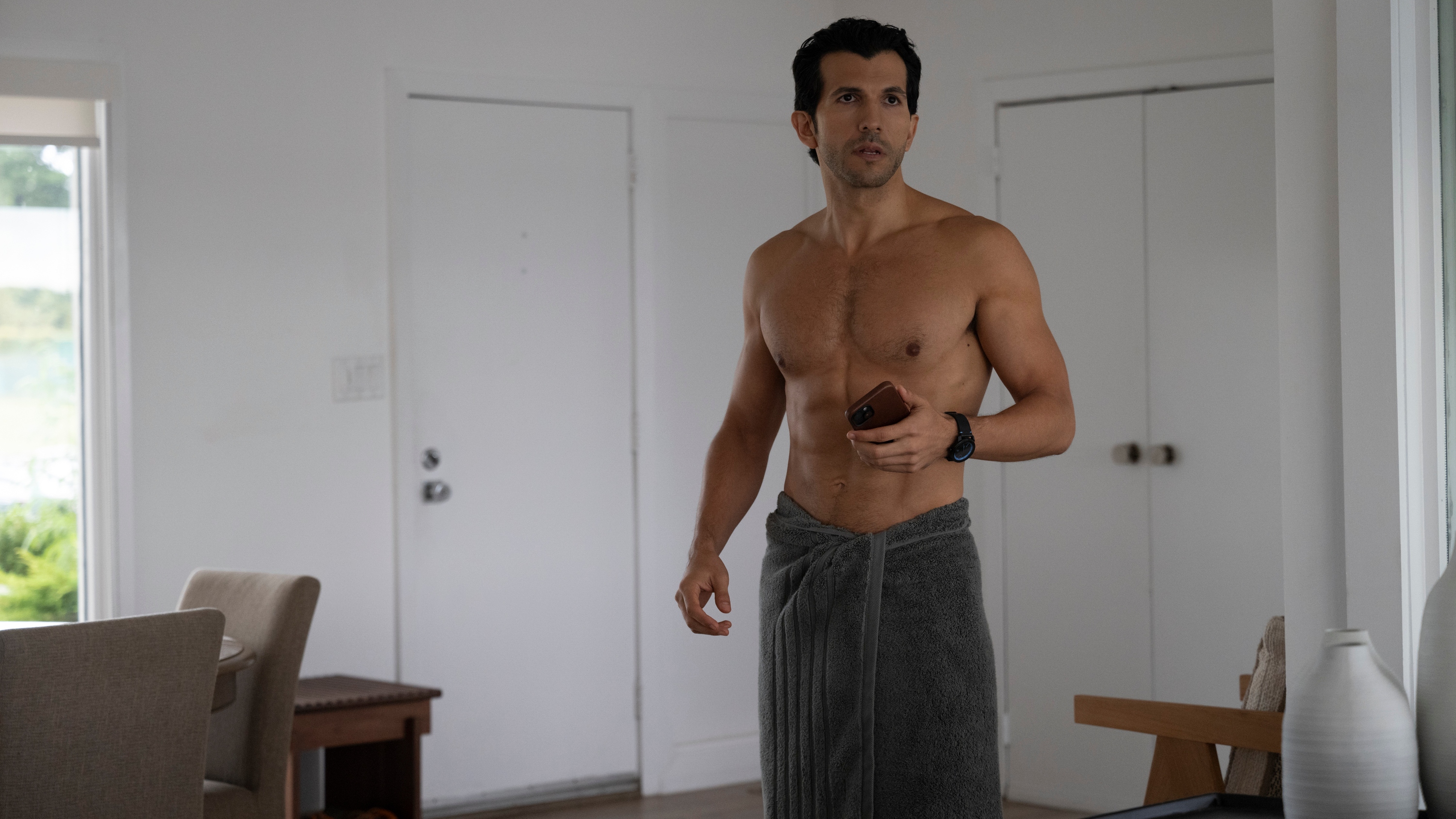 Jake in a white apartment wearing only a towel having only just got out of the shower