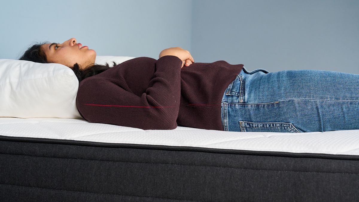Mattress tester Becky George lies on her back on the Plank Firm Luxe mattress in our studio, testing for pressure relief, support and comfort. A red laser line can be seen across her body, indicating the straight line of the spine