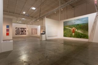 The exhibition space with a large painting on display to the right picturing a grass field and someone standing in it.