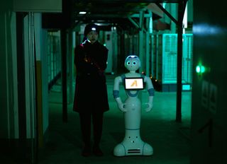 A young woman stood next to a robot in a dark alleyway
