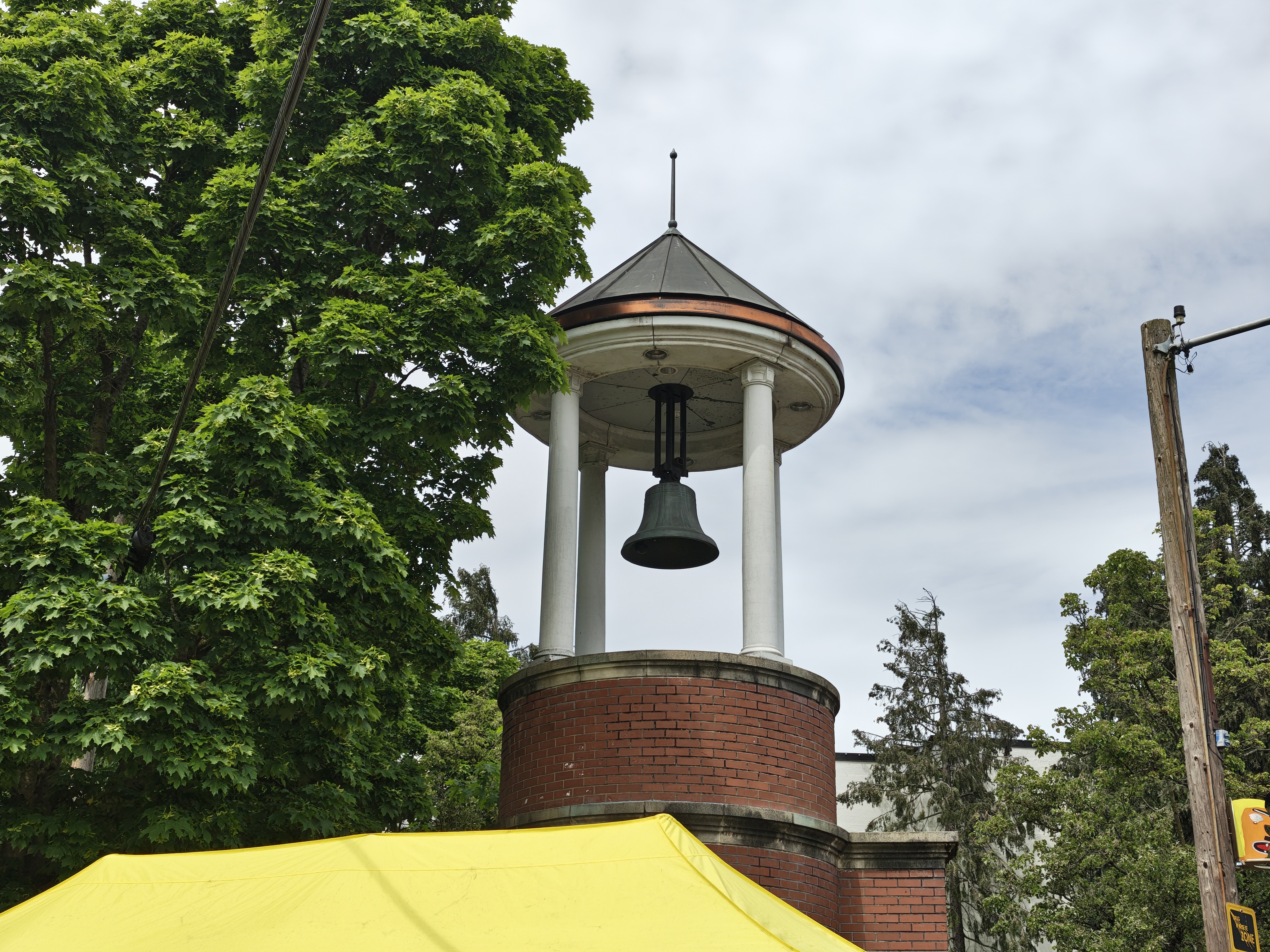 A bell tower next to a tree and a yellow tend