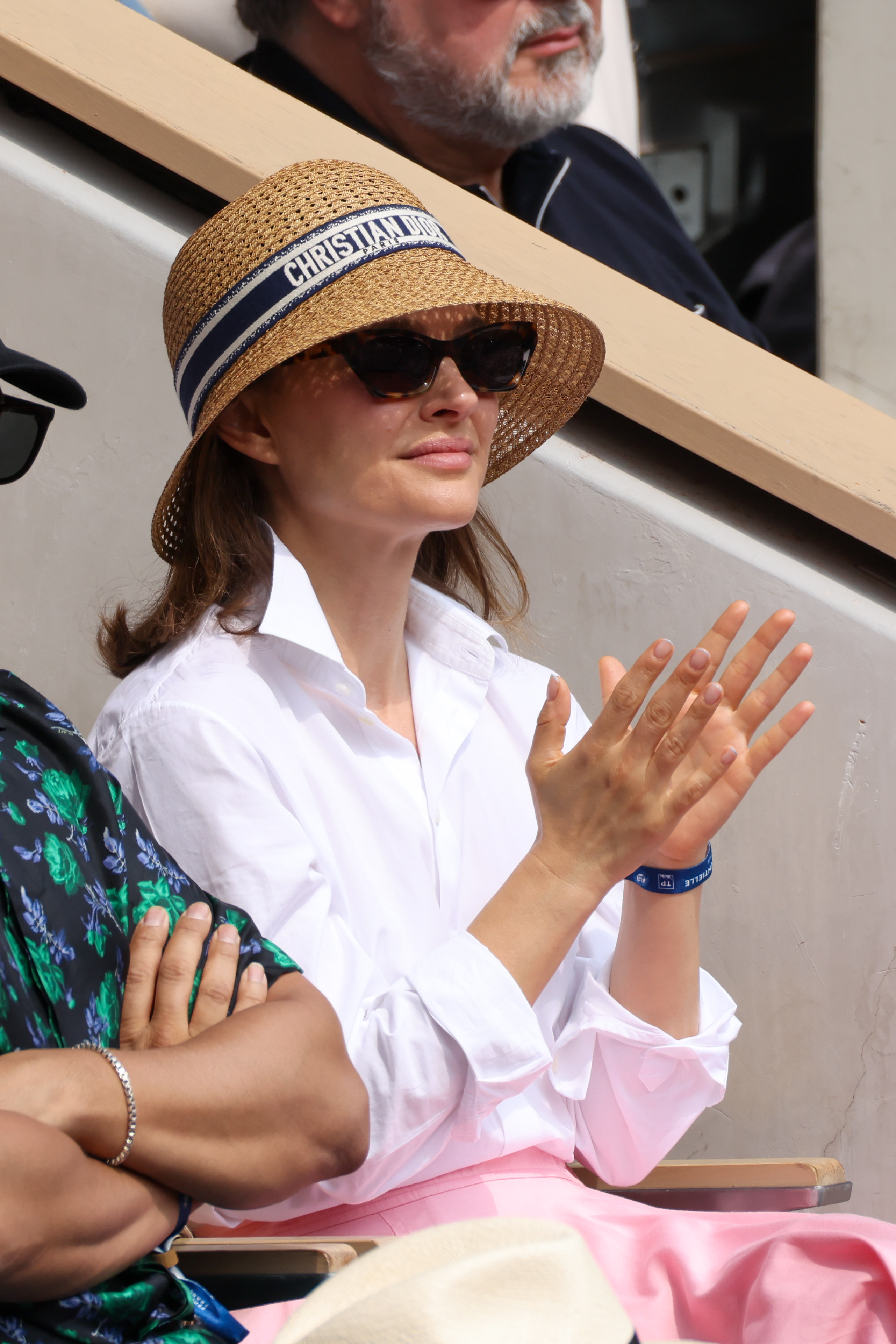 Natalie Portman with a lob haircut wearing a straw bucket hat, a white button up, and a pink skirt.