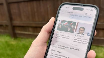 Hand holding an iPhone showing ChatGPT updates on the Iran war.