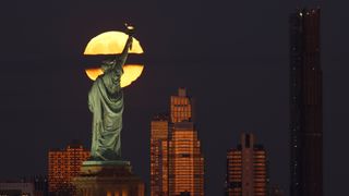The full Hunter's Moon rises behind the skyline of Brooklyn, the Statue of Liberty and the Brooklyn Tower as the sun sets in New York City on October 9, 2022, as seen from Jersey City, New Jersey.