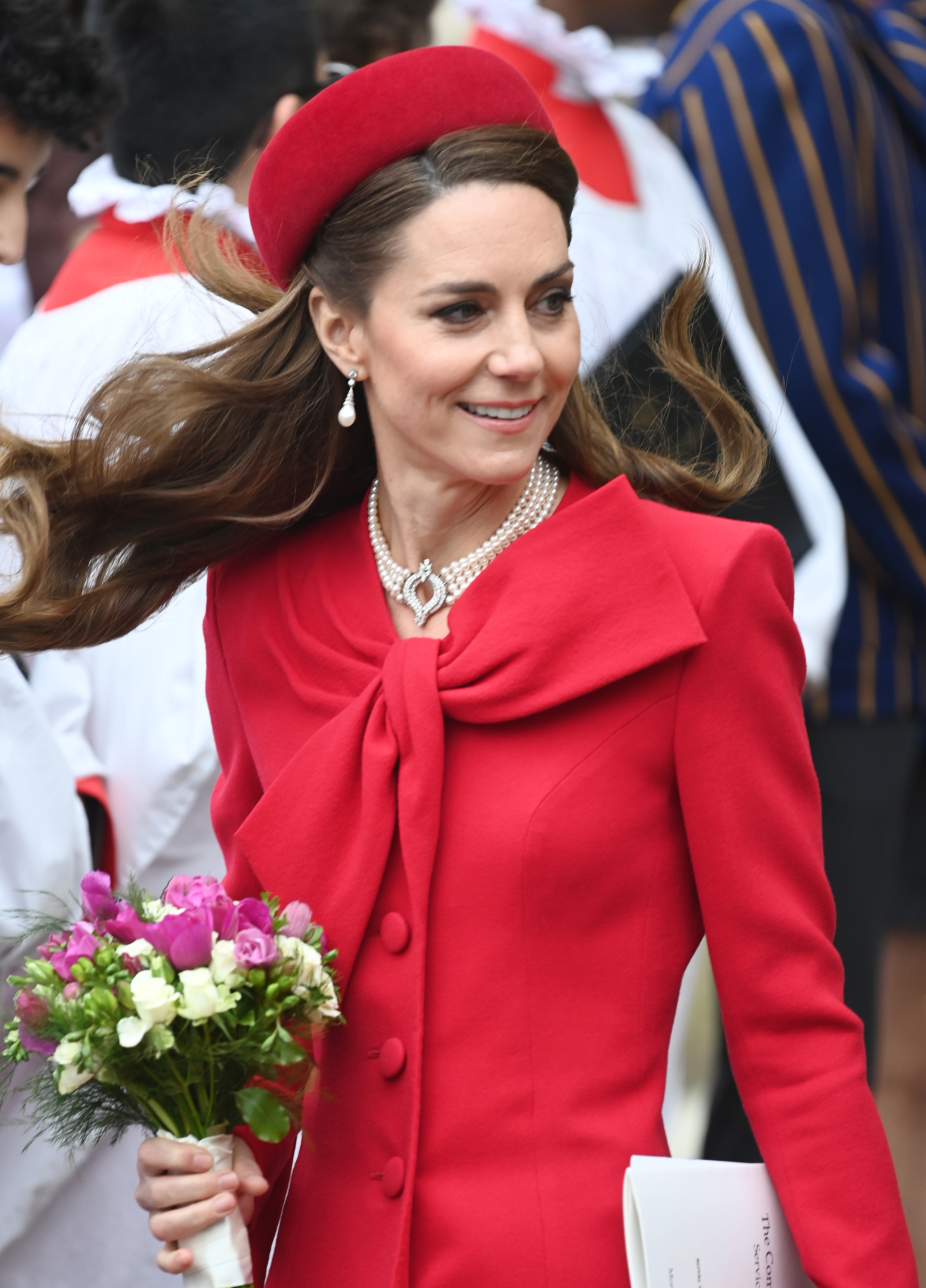 Princess kate wearing a red coat and hat holding flowers