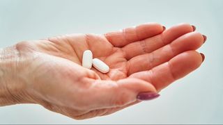 Two white supplement tablets in palm of hand.