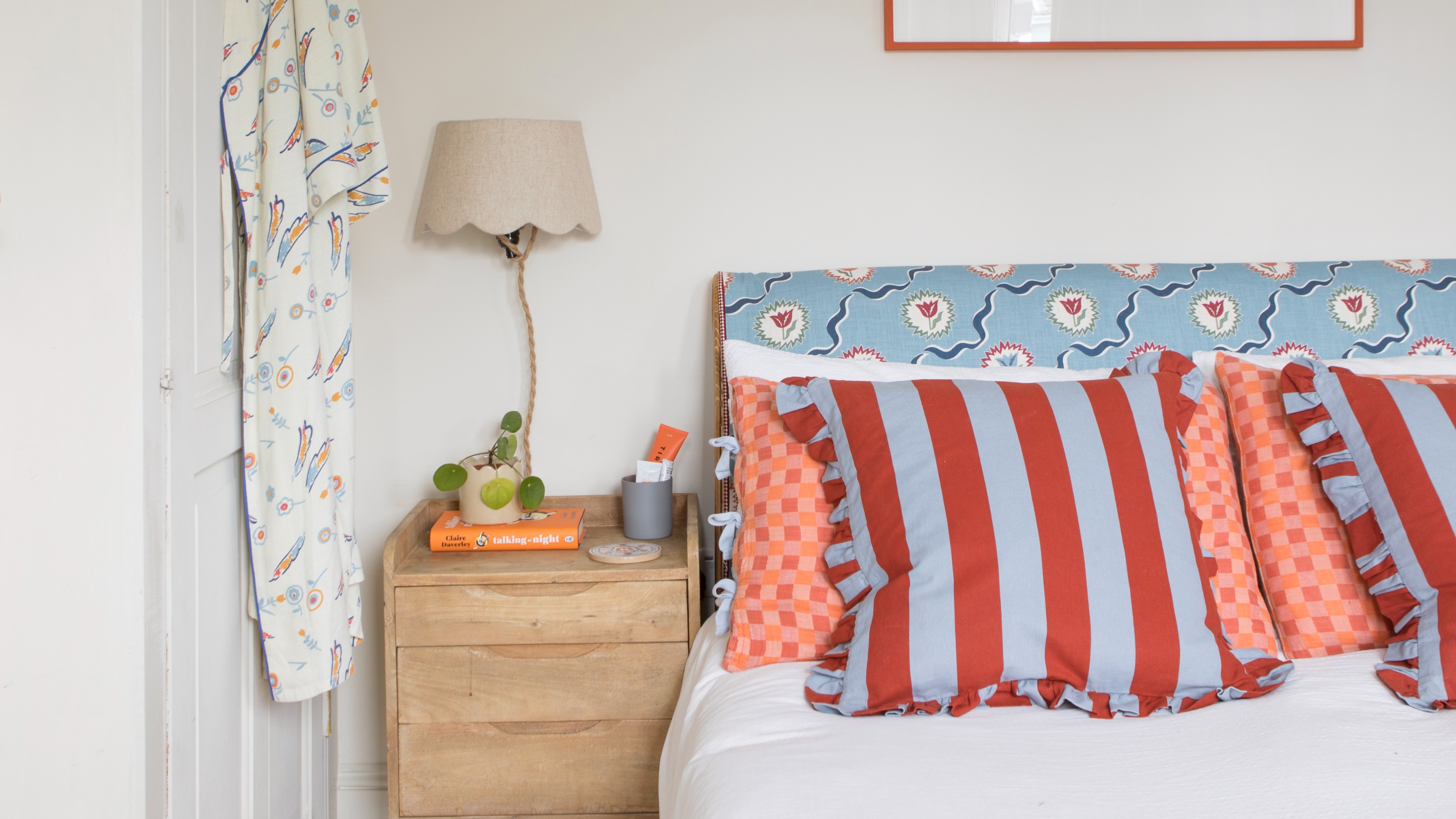 A bedroom with a blue floral-print headboard, chequered pillows and striped ruffled cushions
