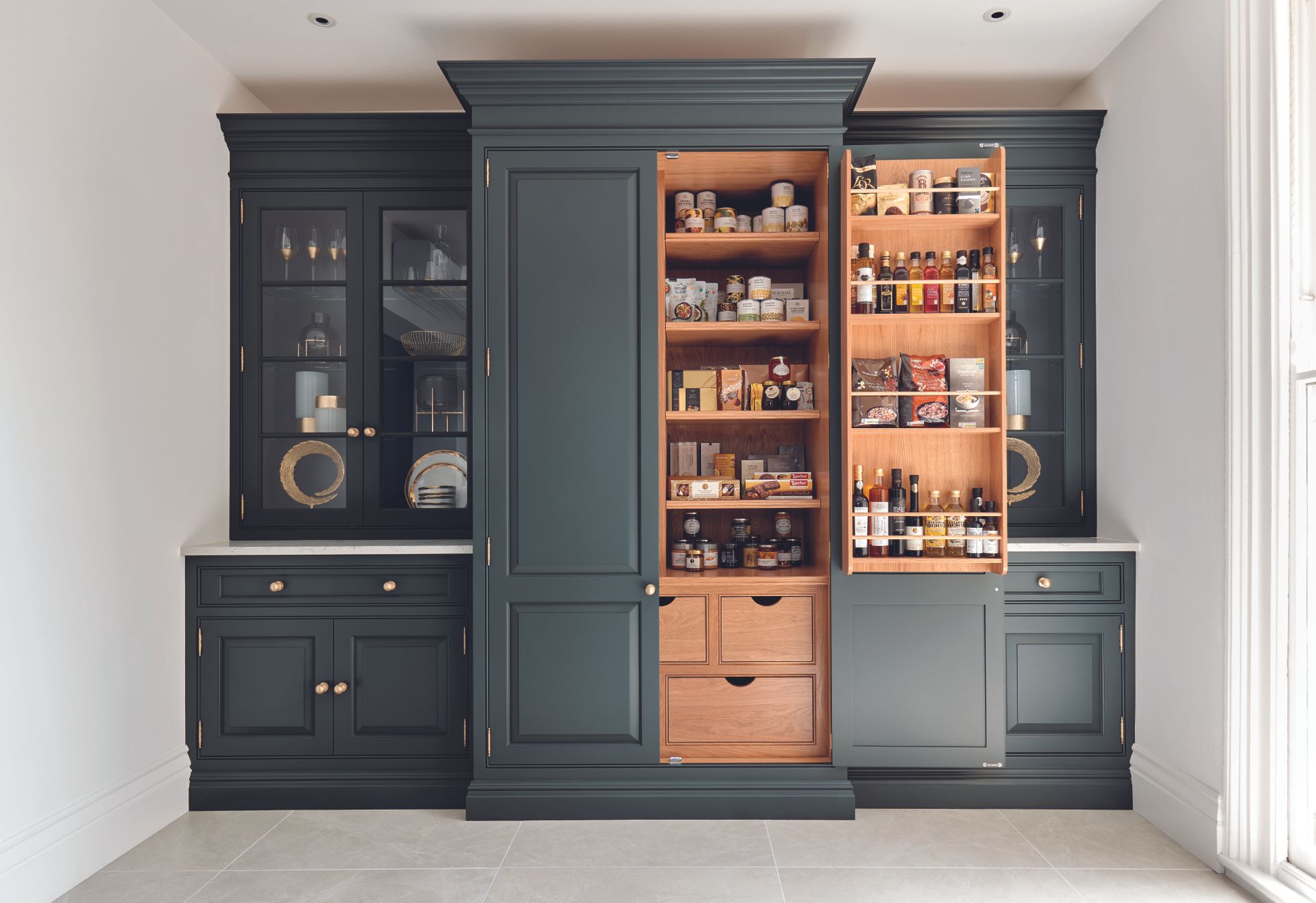 Floor to ceiling kitchen cabinetry in dark blue with larder shelving and glass fronted storage