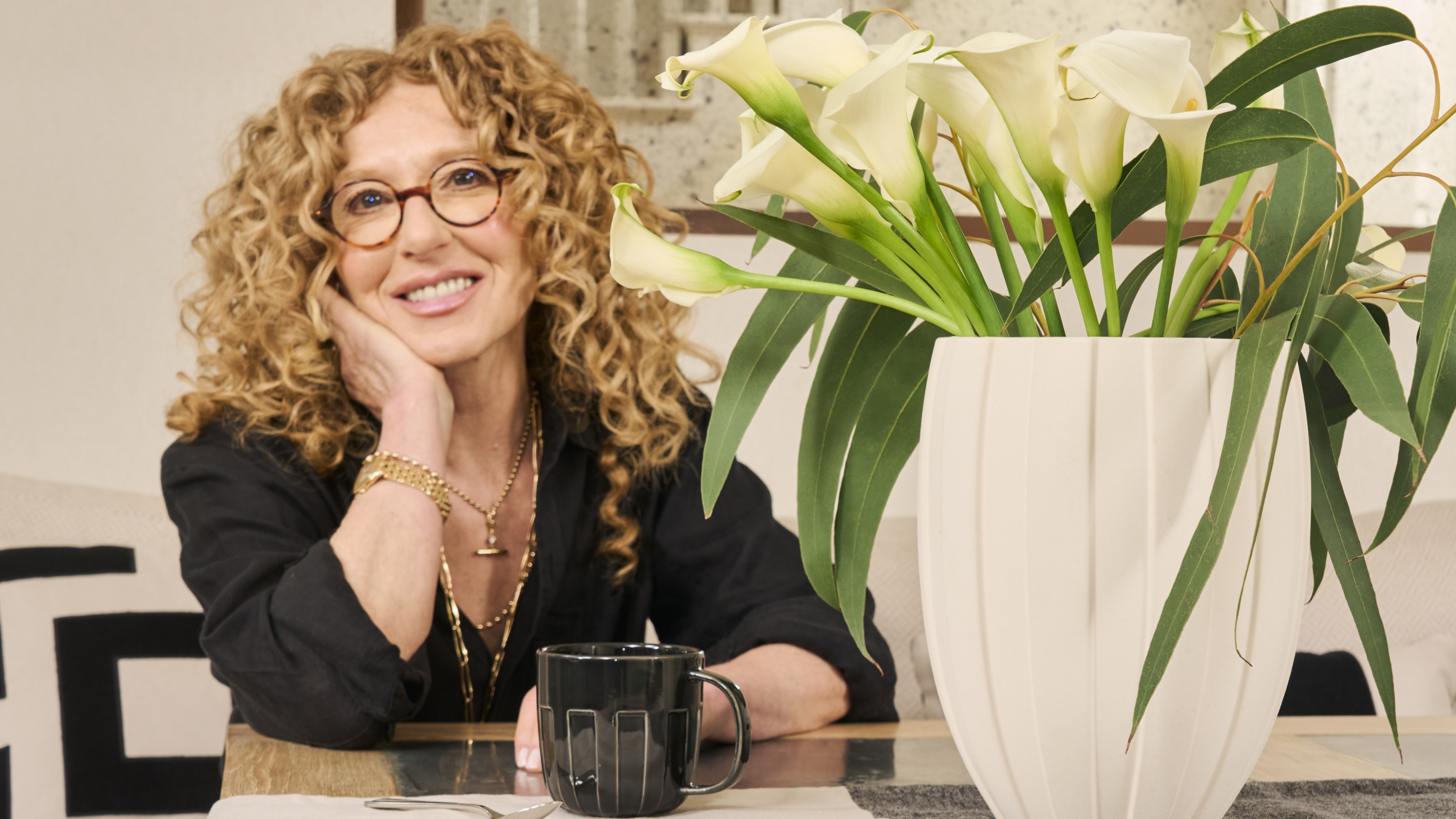 Kelly Hoppen sitting at a table with a vase of her M&S calla lily bouquet next to her