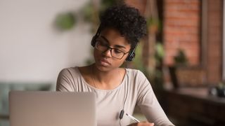 Woman wearing headphones, looking at laptop and making notes