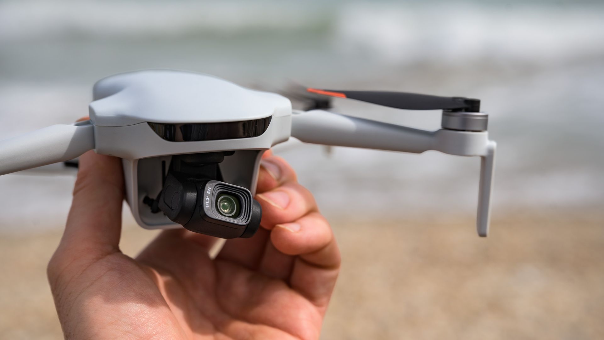 Potensic Atom 3 beginner drone in user's hand, they are in a coastal landscape on a mixed cloudy / sunny day