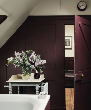 Plum bathroom with vintage cabinet with vase of flowers on it, hint of bath on left, Farrow & Ball