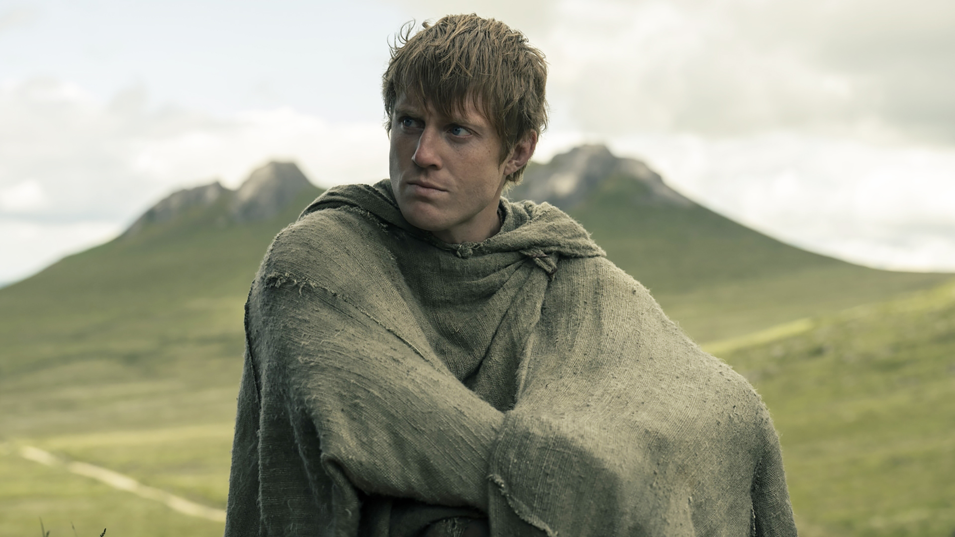 Duncan 'Dunk' the Tall sitting on a hill with his cloak wrapped around him in A Knight of the Seven Kingdoms episode 6