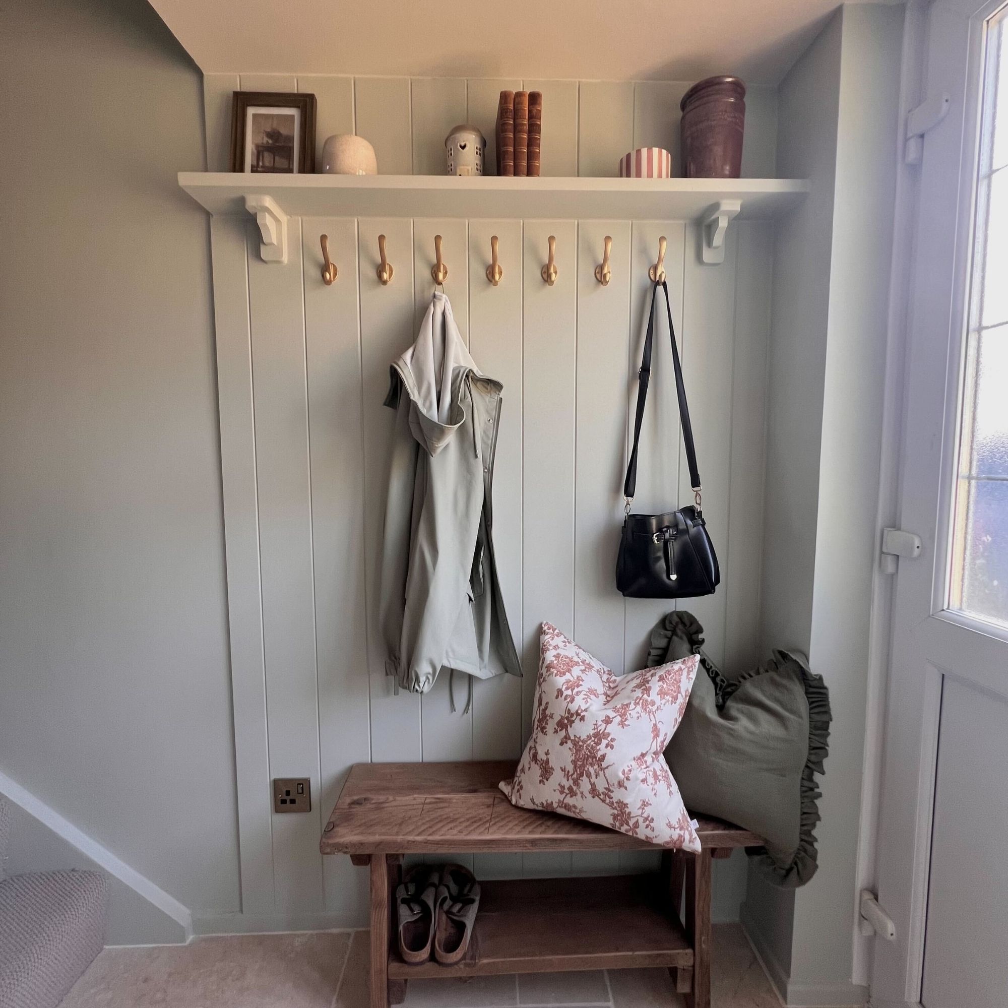 A modern, cottage-core style hallway with a wooden bench, panelling, and accessories.