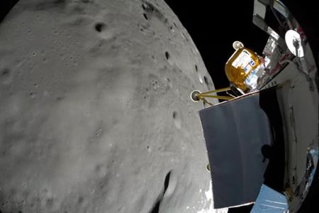 A fisheye view of the moon with a spacecraft to the right of it. There is a yellowish gold box on the craft.