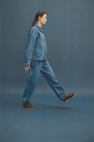 a Still Here model wearing blue jeans, a denim jacket, and brown boots