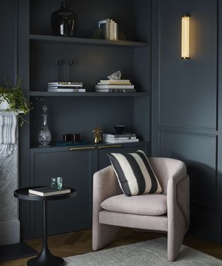 A living room wall lighting idea by Davey Lighitng using their narrow pillar polished brass wall light with navy wall decor, pink chair and shelves