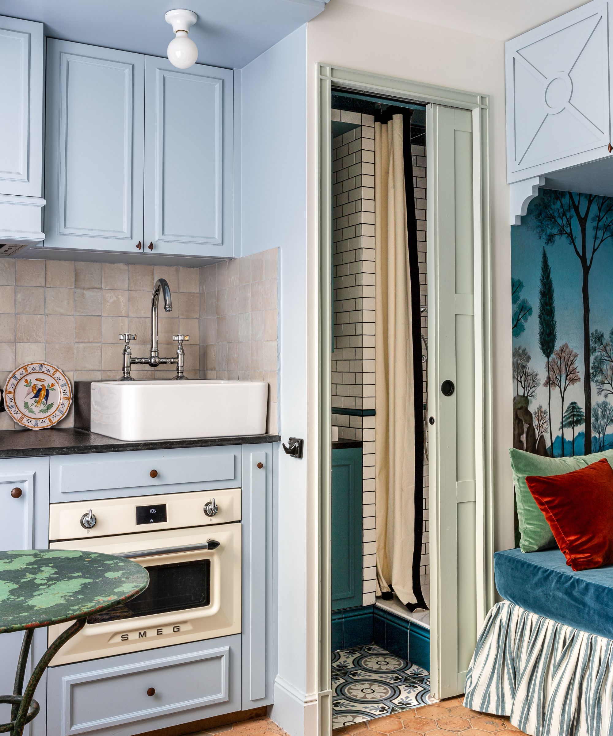 Blue kitchen with daybed in corner looking into bathroom with subway tiles