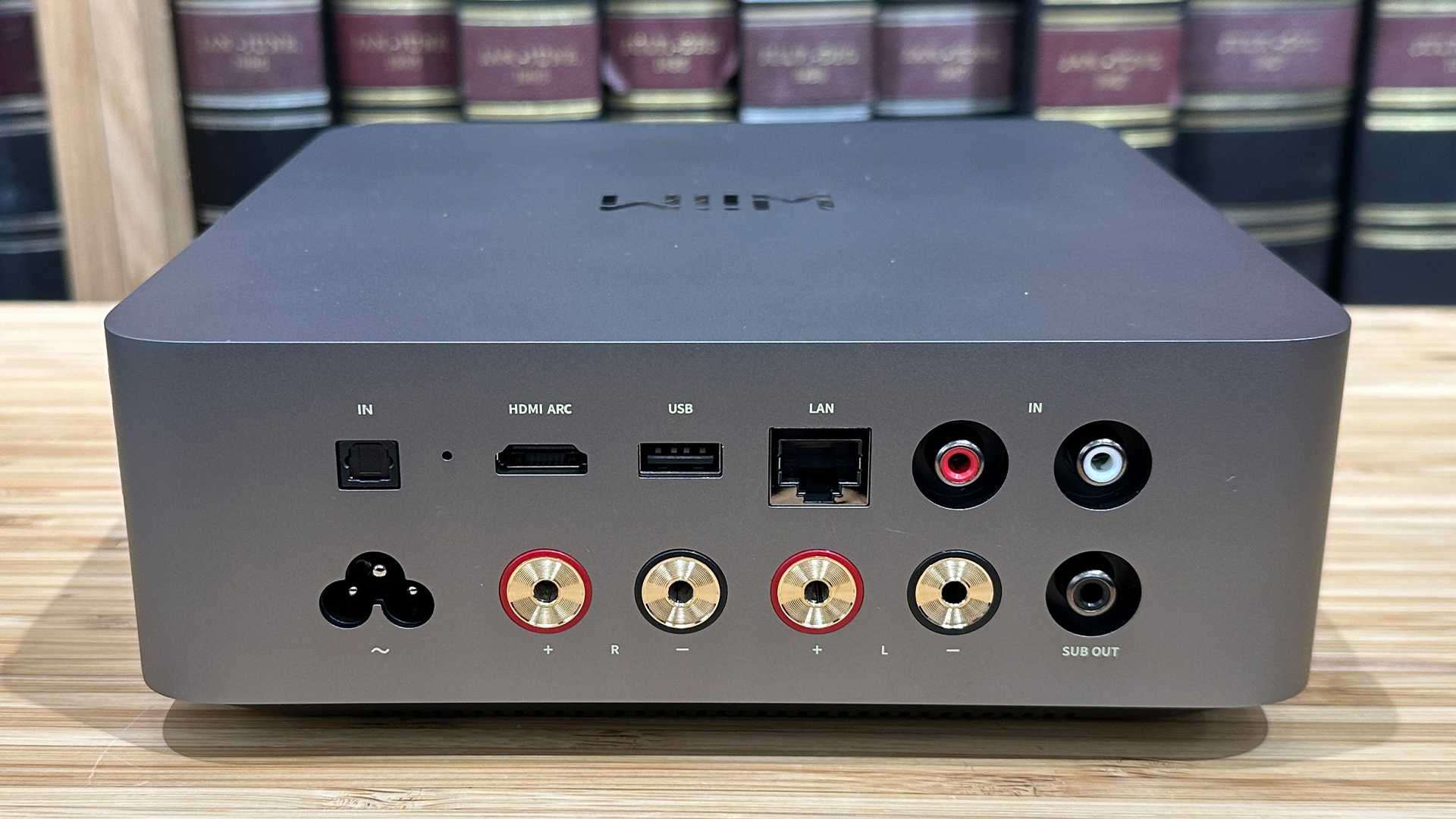 WiiM Amp Ultra streaming amplifier on wooden hi-fi rack in front of bookcase rear of unit showing connections
