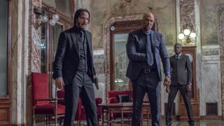 John Wick stands alongside a fellow assassin, with the pair looking angry, in one of John Wick's movies