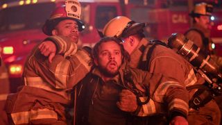 Jake and another firefighter holding Bode back as he looks at a burning building.