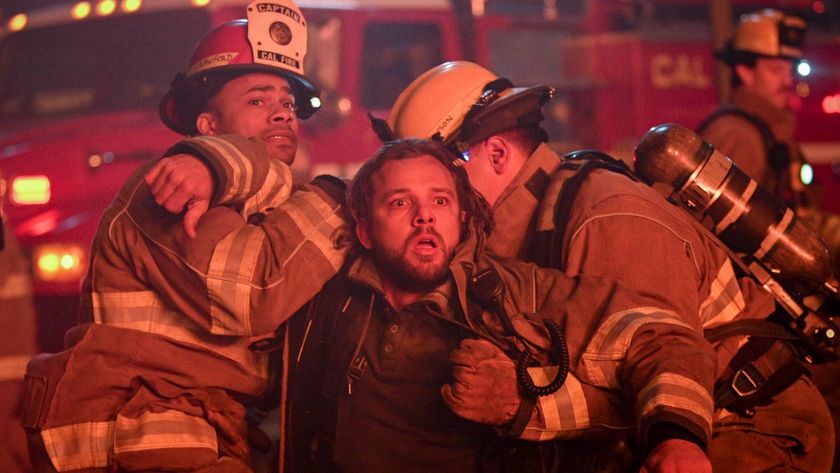 Jake and another firefighter holding Bode back as he looks at a burning building.