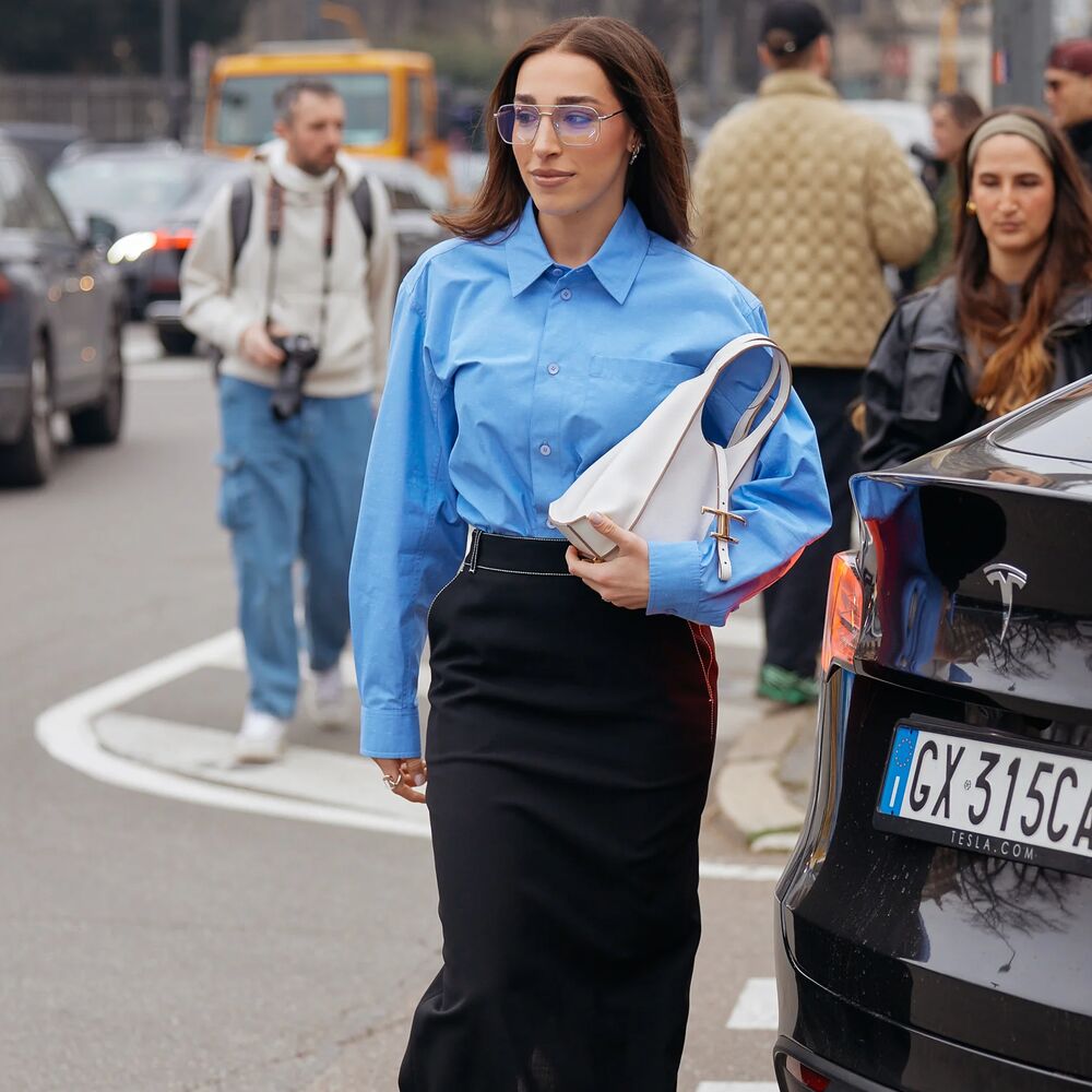 Woman wears button down, black pencil skirt, white handbag, and black heels.