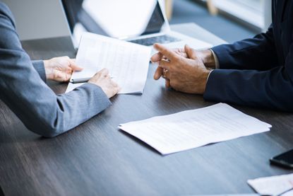 The camera focuses on documents being reviewed by two people. We only see their hands on a desk.