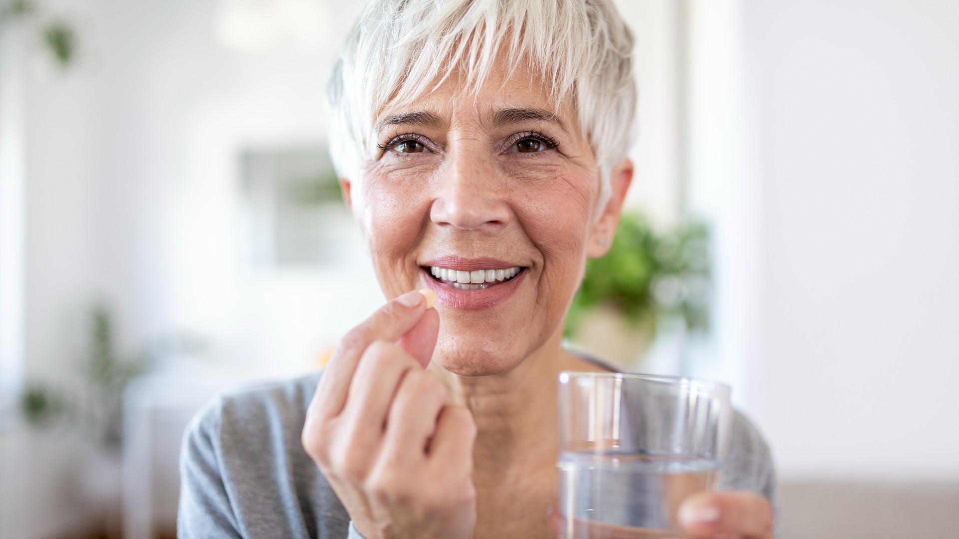 Souriant heureux sain d'âge moyen femme de 50 ans prenant un complément alimentaire vitamine pilule avec un verre d'eau à la main