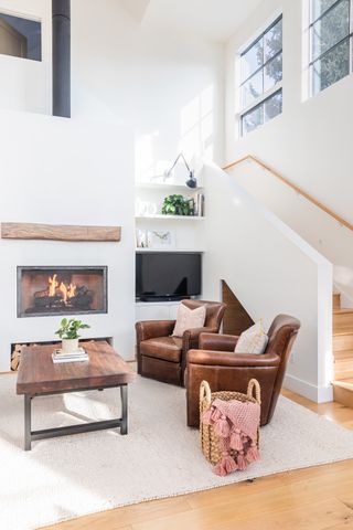 A contemporary lounge area with cassette fireplace, wooden coffee table, brown leather armchairs and built-in TV