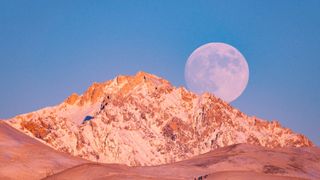 the moon rises over a large snow-covered mountain
