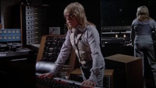 Paul Williams stands at a control panel with a curious look in Phantom of the Paradise.