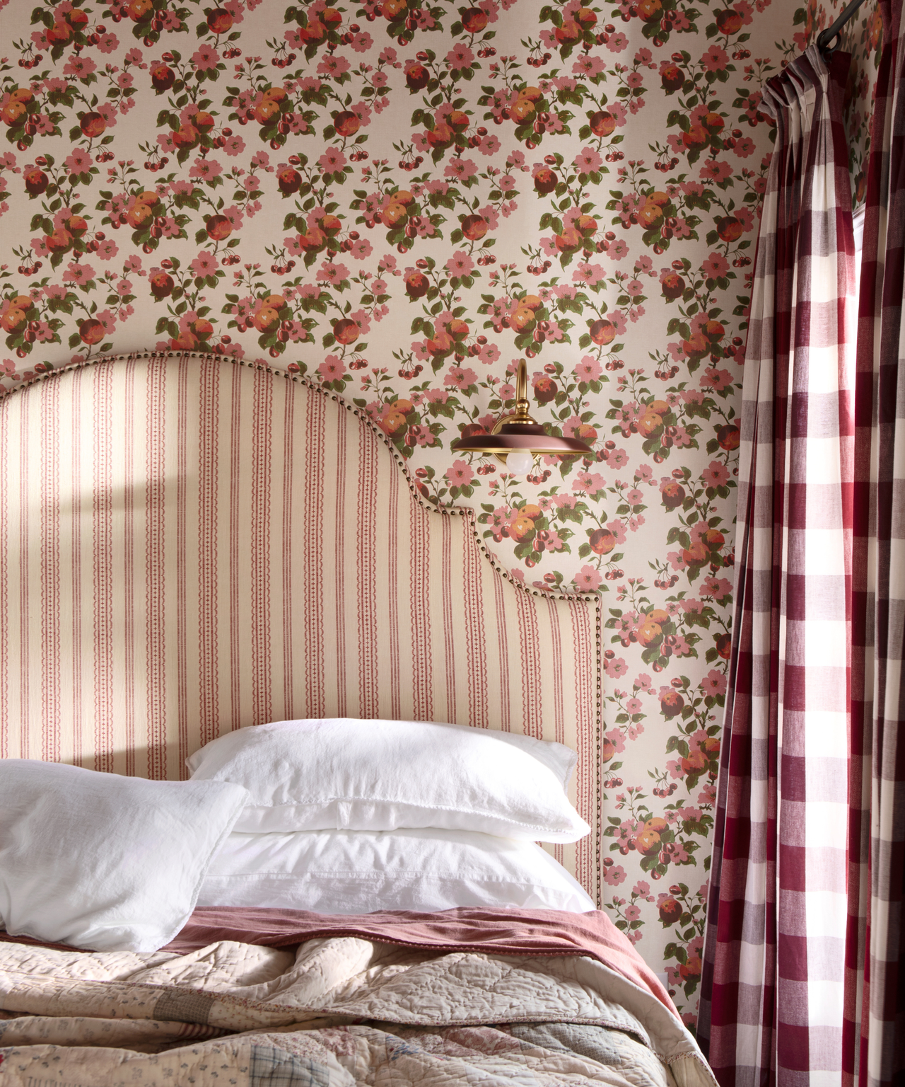 a bedroom with red floral wallpaper, gingham drapes, and a striped red headboard
