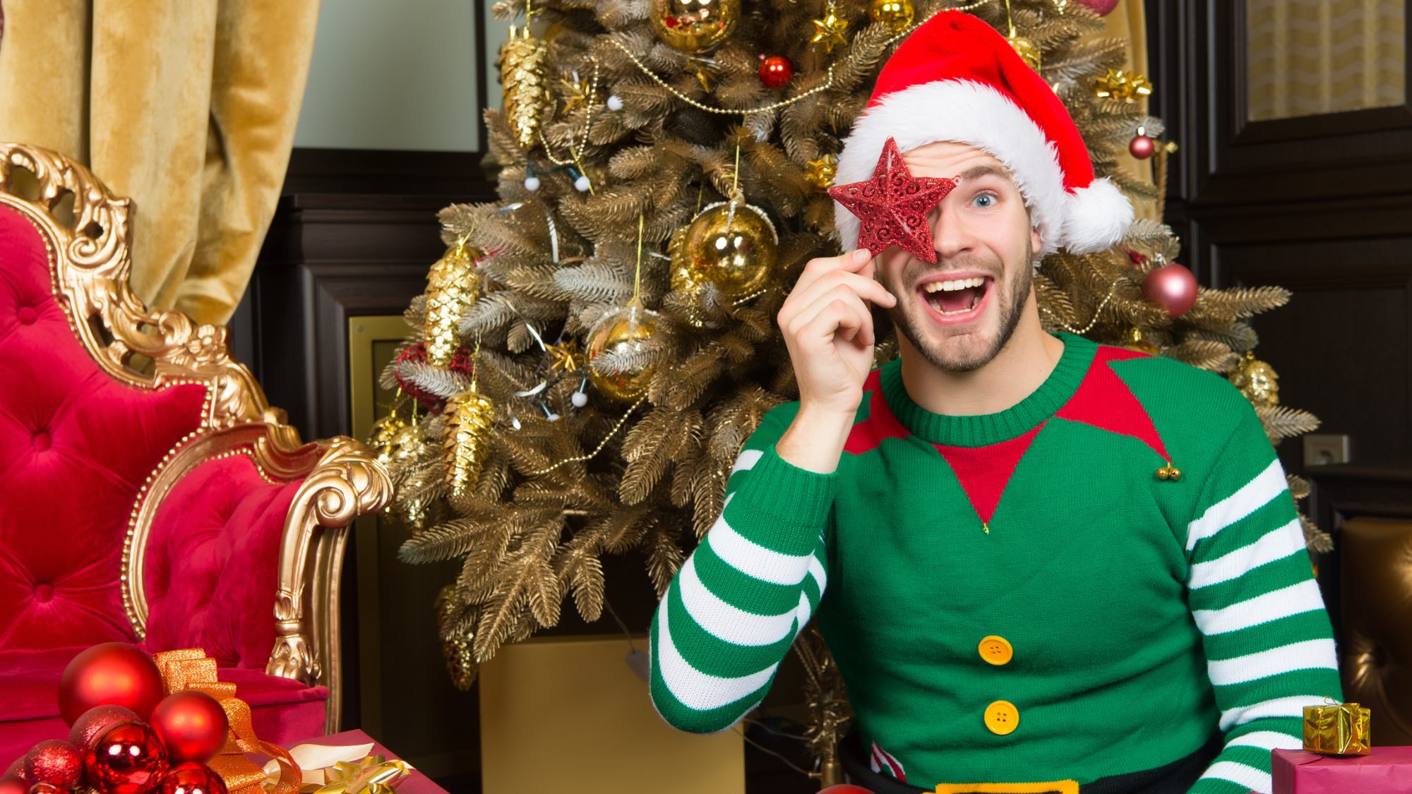 man dressed as elf in front of christmas tree