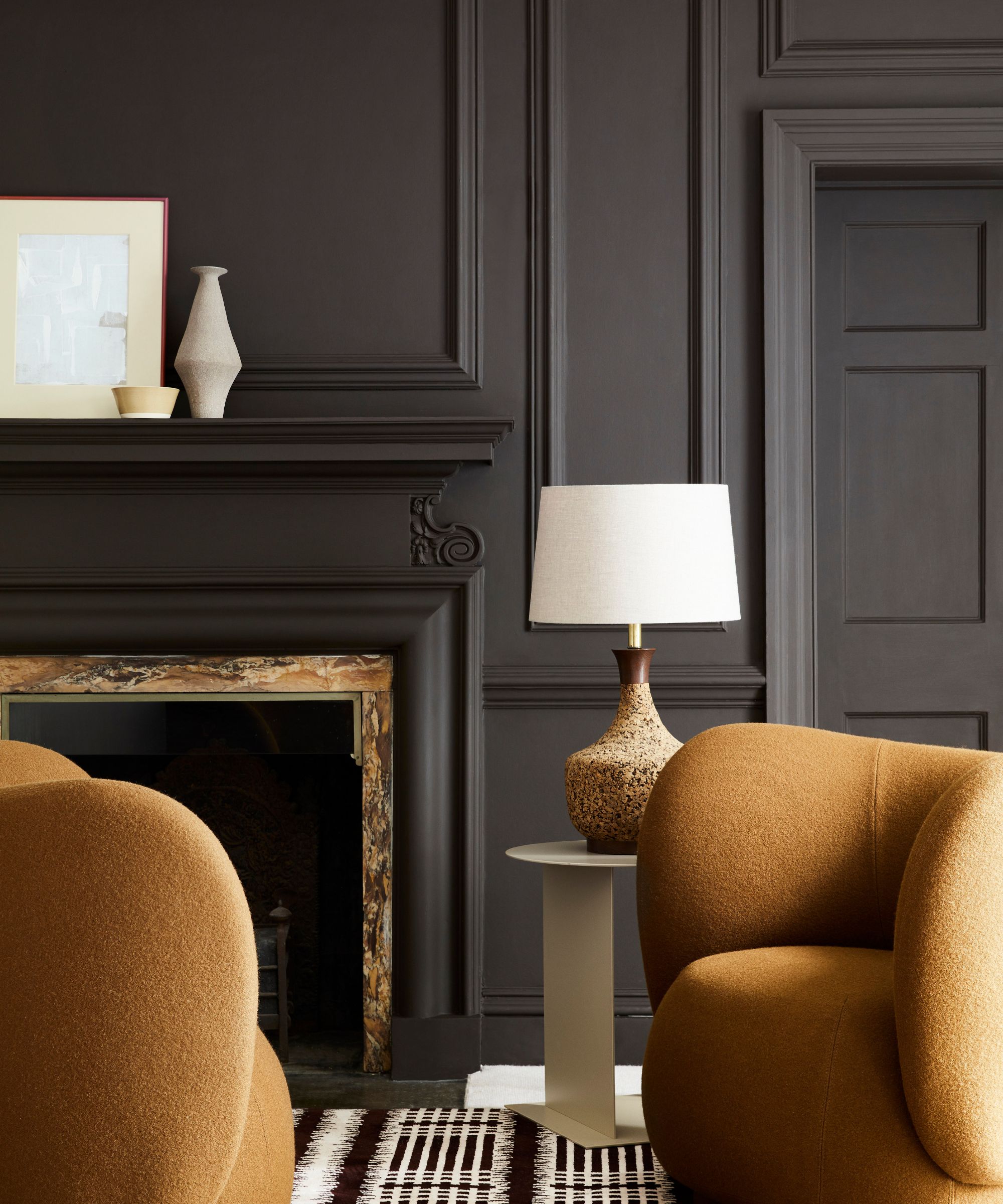A formal living room with black walls and dark yellow armchairs in front of a fireplace.